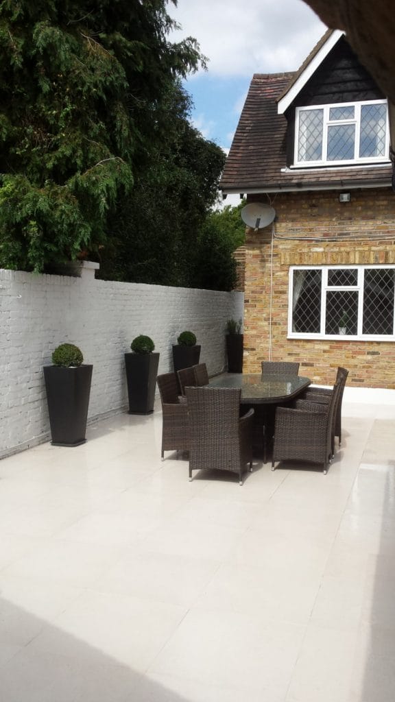 Outdoor table and chairs on a pale paved patio beside a brick house