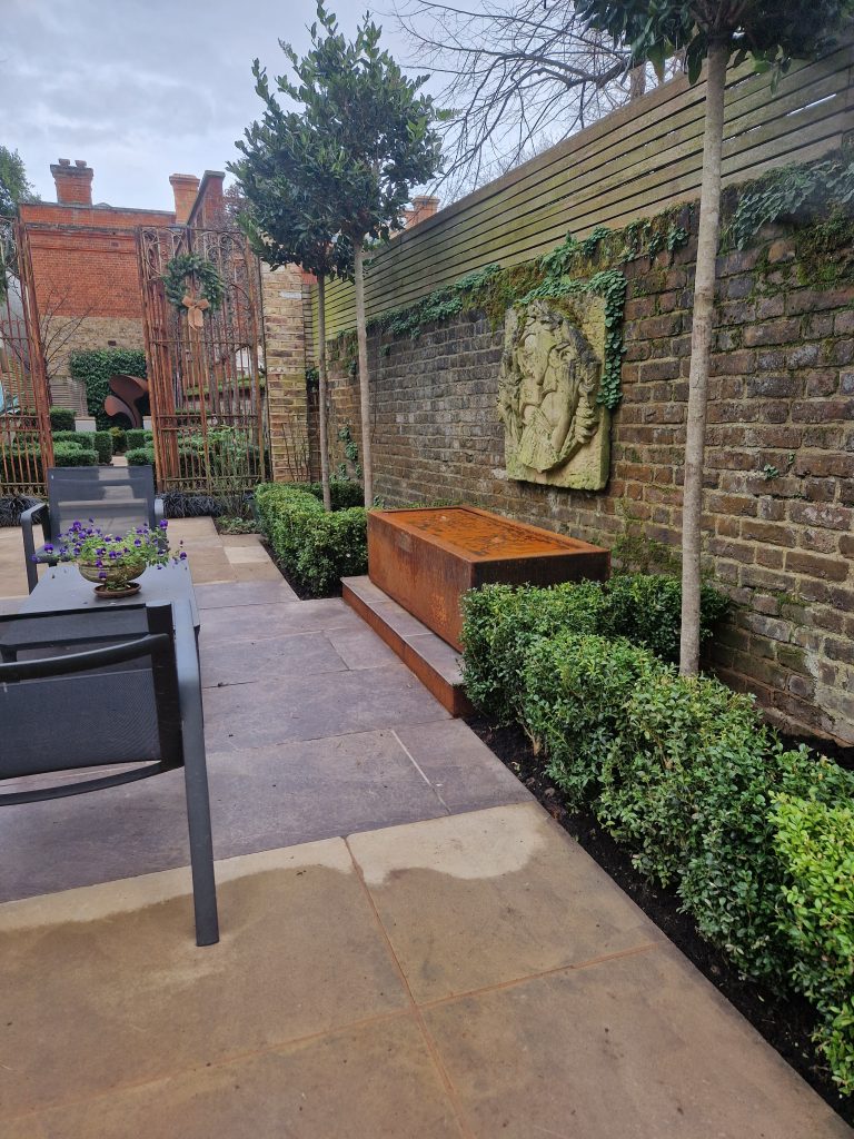 Corten-steel water feature and paving alongside a brick garden wall. Richmond Garden Design.