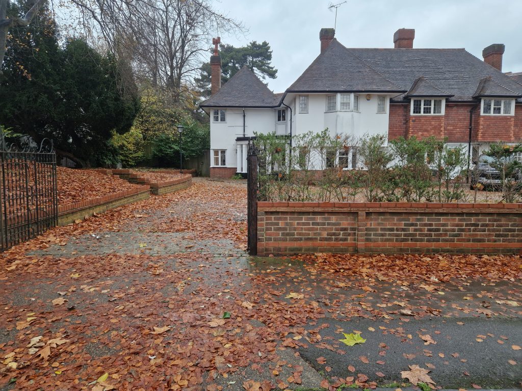 Front garden with brick-edged raised beds and a driveway covered in autumn leaves