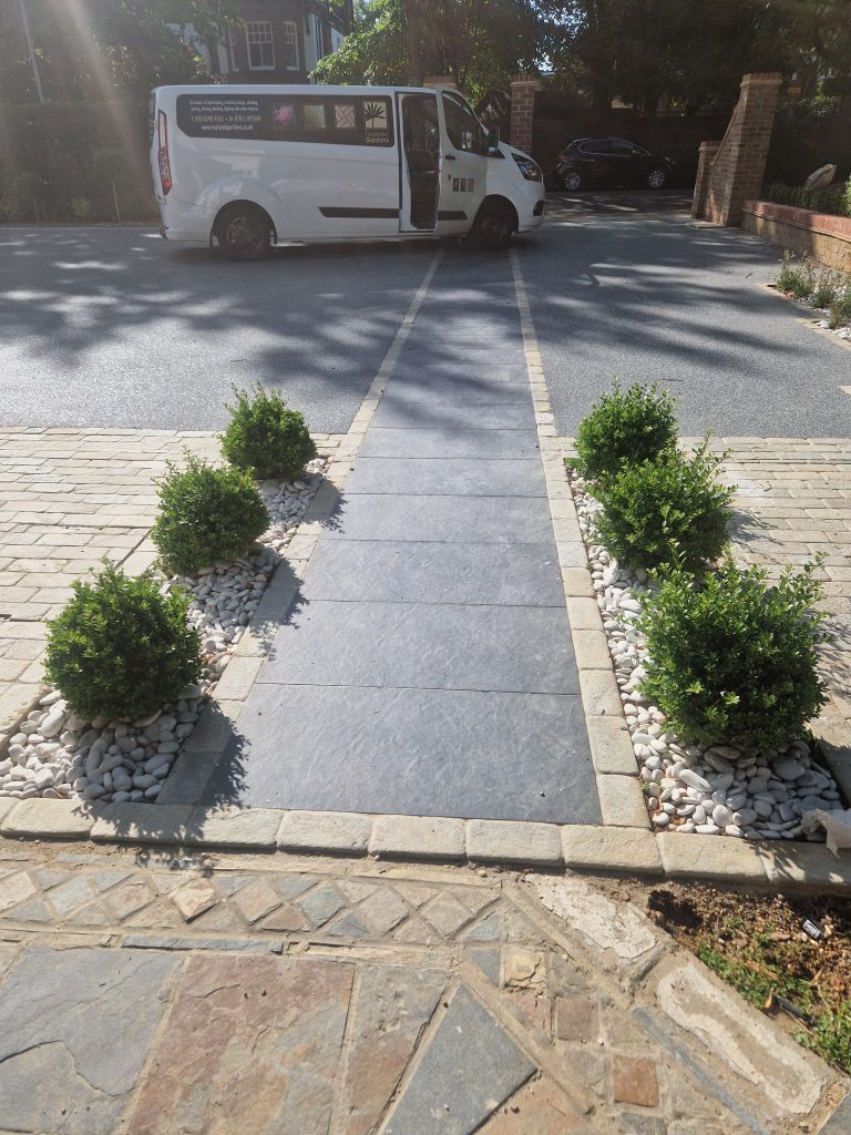 Standing slate stones set in white pebbles with brick wall planting