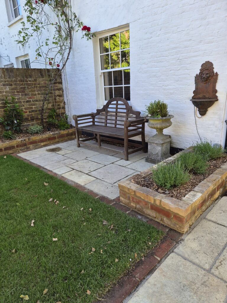 Timber bench on a paved seating area beside a white house and raised planting bed