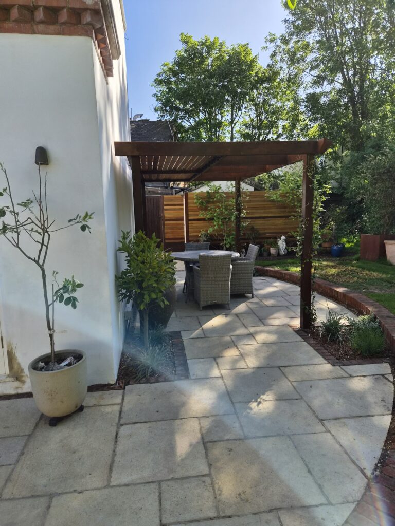 Curved paved patio with a timber pergola and dining set beside a white rendered house